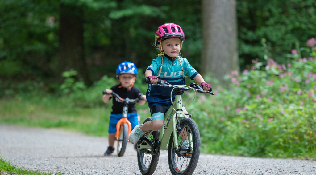 Zwei Kleinkinder fahren auf ihren Cube Kinderfahrrädern auf einem Weg durch den Wald