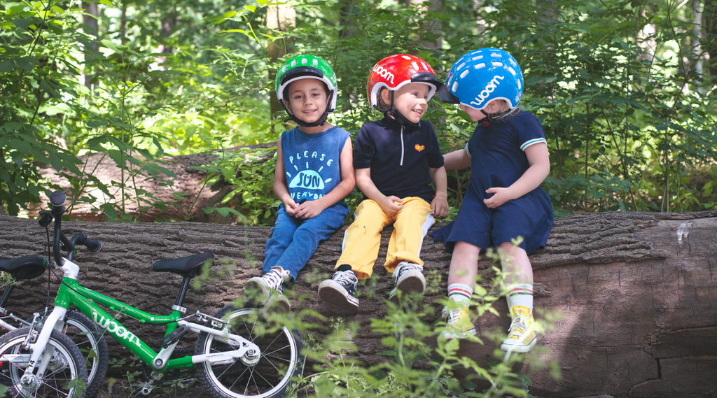 Drei Jungs sitzen auf einem Baumstamm im Wald neben ihren Woom Kinderfahrrädern