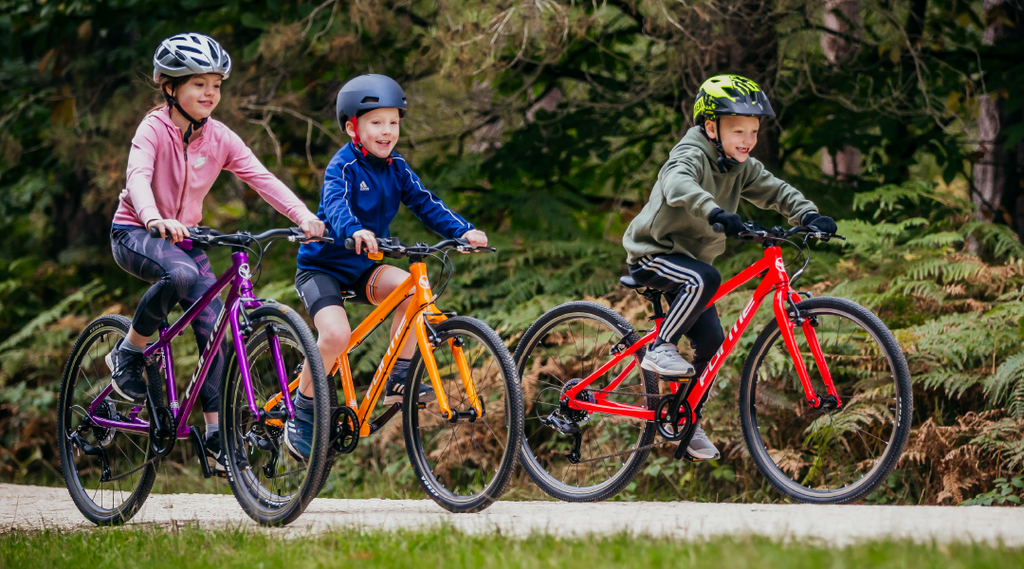 Drei Teenager fahren auf ihren bunten Forme Kinder Kinderfahrrädern auf einem Waldweg
