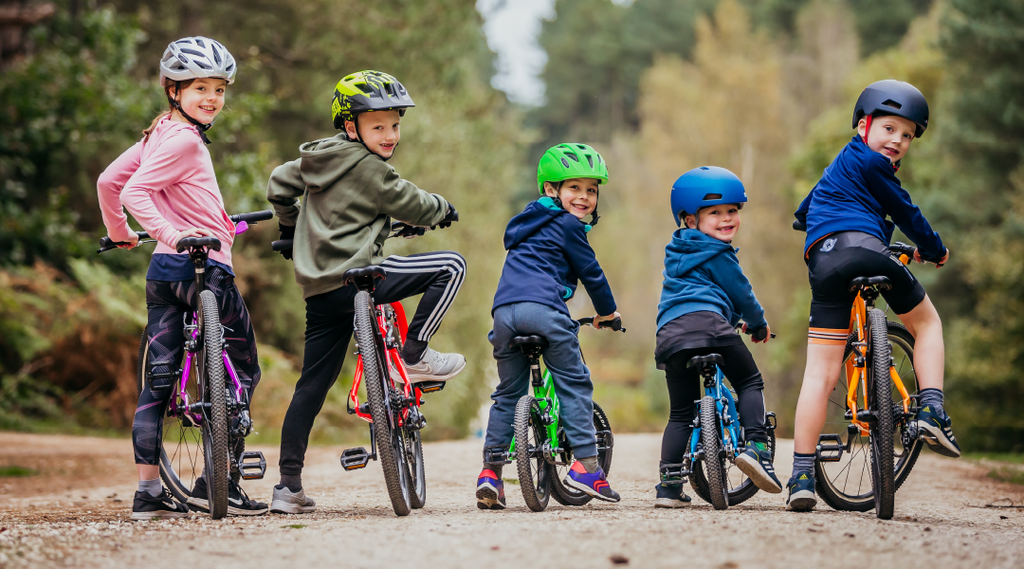 Fünf Kinder stehen umgedreht mit ihren Forme Kinderfahrrädern im Wald und drehen sich zur Kamera