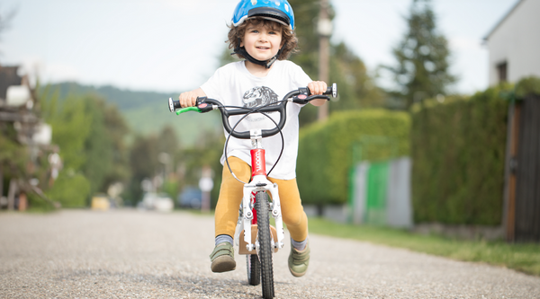 Ein kleiner lachender Junge fährt auf einem leichten roten Laufrad Woom 1 Plus