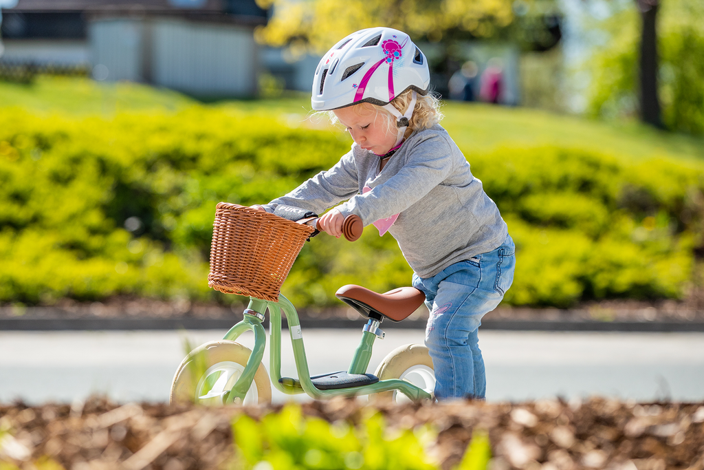 Kleines Mädchen mit Fahrradhelm schiebt Puky LR M in Grün