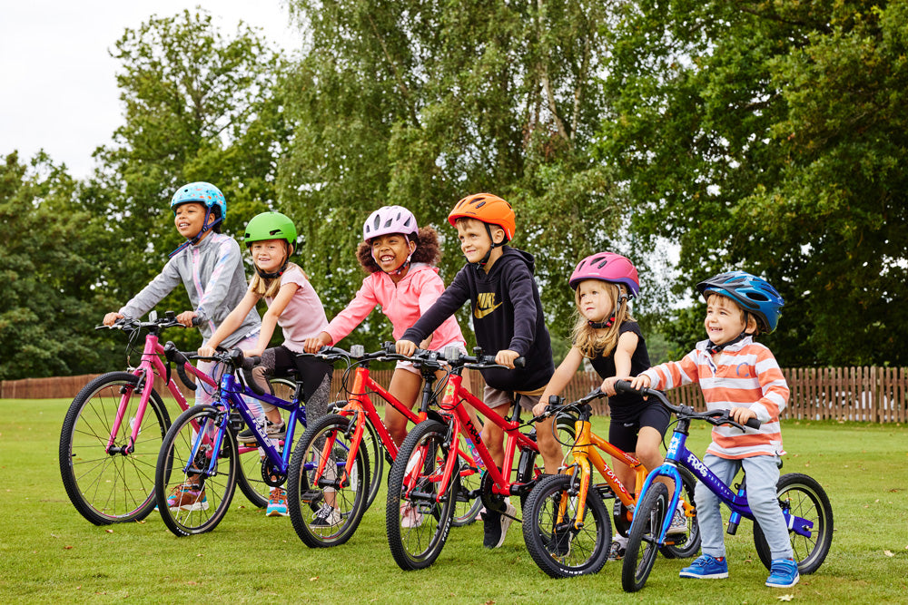 Fröhliche Kinder auf leichten Kinderfahrrädern von Bike Club in allen Größen auf einer Wiese im Freien