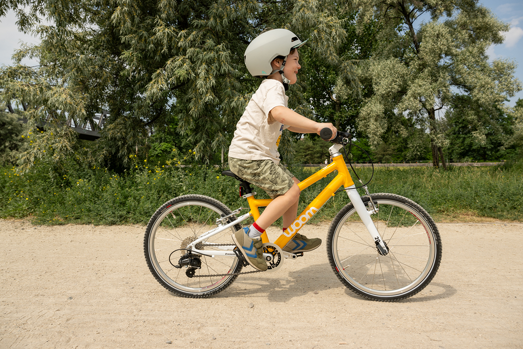 Junge fährt mit gelbem Woom Kinderfahrrad durch den Park