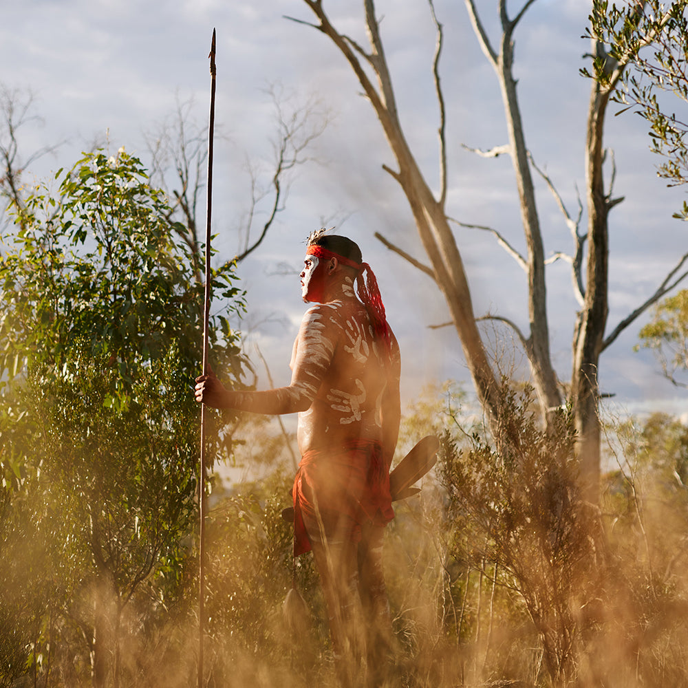 First Nations Man in traditional dress standing in bushes