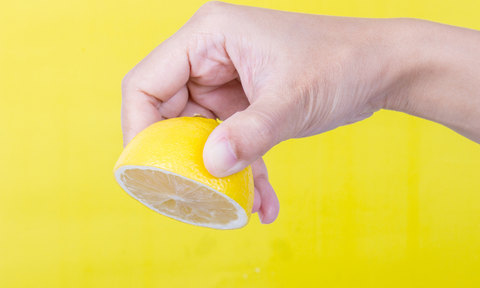 A hand squeezing a lemon against a yellow background