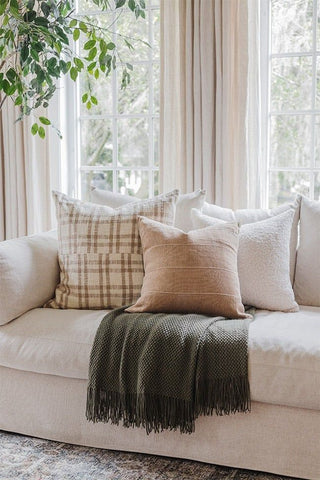 Cream couch with a green throw blanket and three pillows. One white, one tan, and one tan with brown plaid
