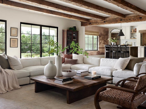 A living room with a large cream colored sectional, wooden coffee table, and exposed wood beams.