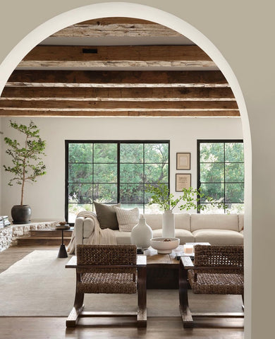 A cream colored living room with exposed wood beams and white and wicker furniture.