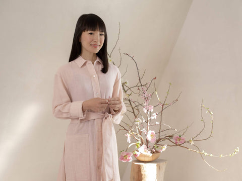 Marie Kondo standing in front of a large, pink indoor plant.
