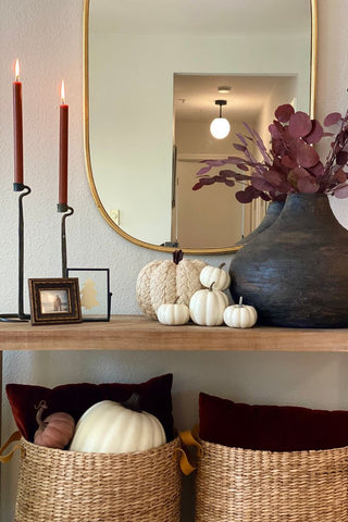 Console table with two maroon candles, decorative cream pumpkins, and black vase with burgundy plant stem