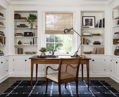 Home office with white walls, built-in shelves, a dark wood desk, and a navy rug underneath