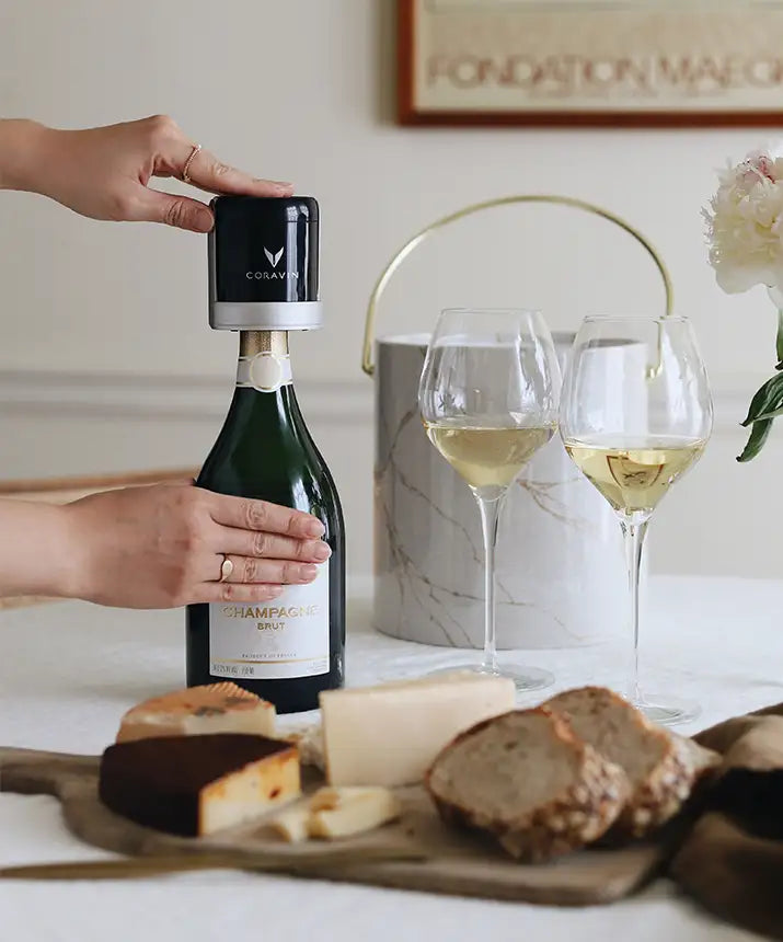 Lifestyle image of a person placing the Sparkling Stopper on top of a bottle of wine, next two two glasses of white sparkling wine, a charcuterie board, and an ice bucket.