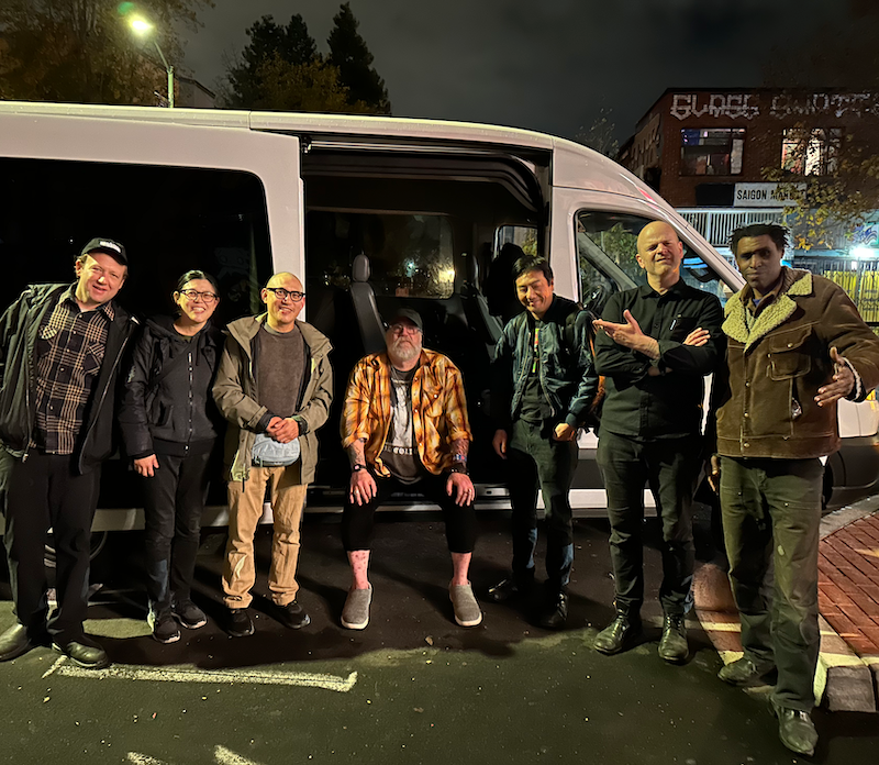 Left-to-right: Shaun Wagner (Acharis), Yvonne Chen, George Chen, Andee Connors, Warren Ng, Marc Kate, Marshall Trammell standing outside the van on Telegraph Avenue Oakland outside the Stork Club
