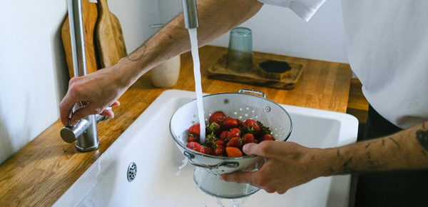 A man turning on a kitchen faucet to wash fruit