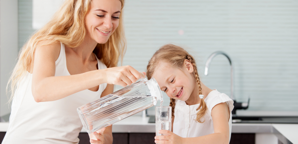 A mother pouring a glass of fresh filtered water for her young daughter