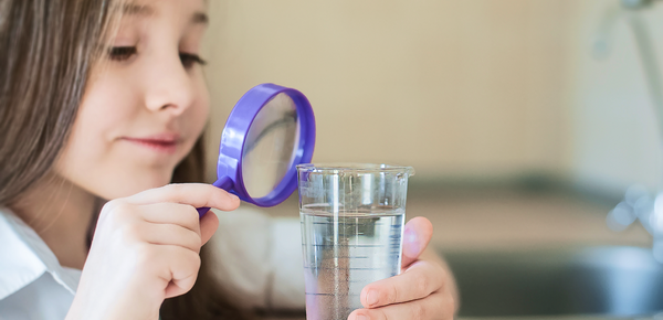 A young girl inspecting a glass of water with a magnifying glass