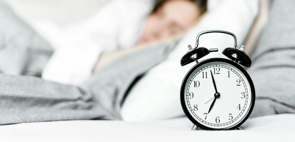 An alarm clock on bedside near a sleeping woman