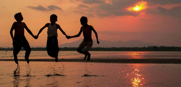 Children holding hands a jumpng in shallow water