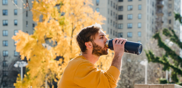 A man in the city drinking water from a metal bottle