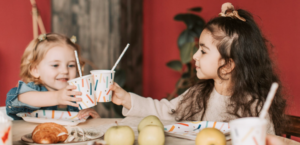 Two kids drink from party cups with straws