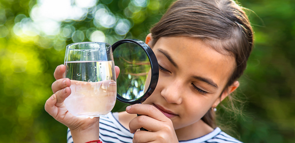 A young girl inspecting a glass of filtered water with a magnifying glass
