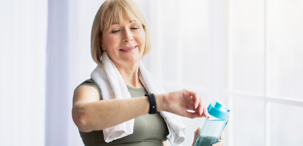 An older woman holding a bottle of filtered water checks her heart rate