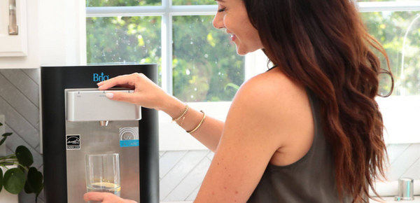 A woman filling a glass with fresh filtered water from a Brio countertop cooler