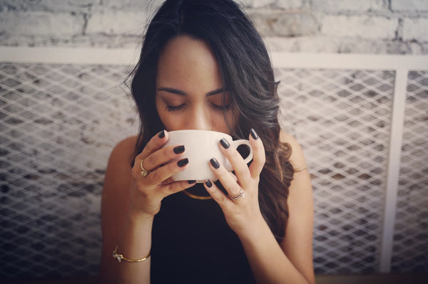 La mujer se sentó bebiendo una bebida caliente con ambas manos ahuecando la taza.