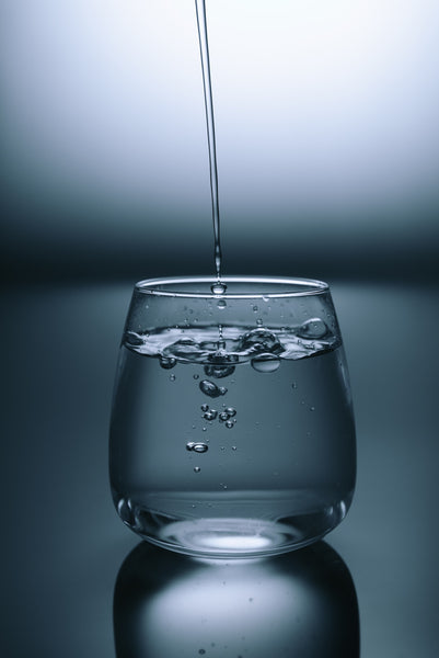 vaso de agua pura filtrada con un pequeño chorro de agua todavía cayendo