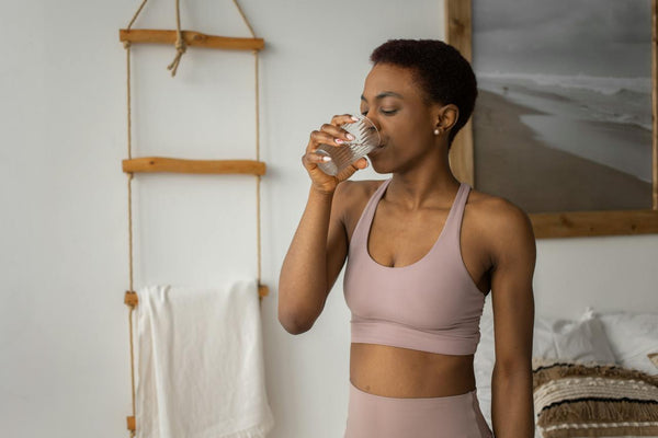mujer en equipo de entrenamiento bebiendo un vaso de agua en su casa