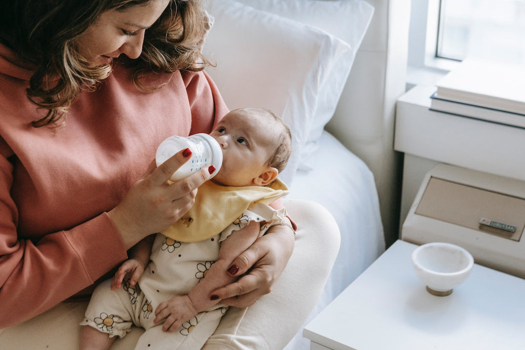 Mujer alimentando a un bebé con leche de fórmula embotellada mientras estaba sentada en el borde de una cama