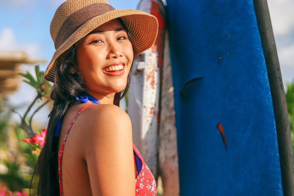 Hawaiian beauty in straw hat stands by surfboard