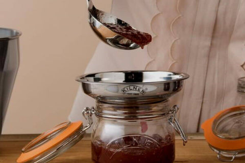 Person ladling freshly made jam into a wide-mouth preserving funnel over a jar