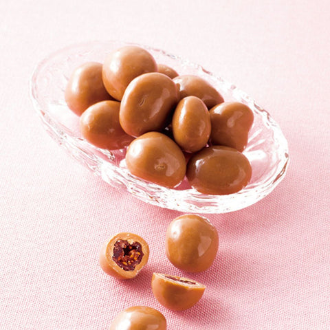 Image shows chocolate-coated cranberries in a bowl with pink background.