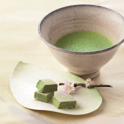 Image shows green tea chocolate blocks on a plate and a cup of tea on the side.