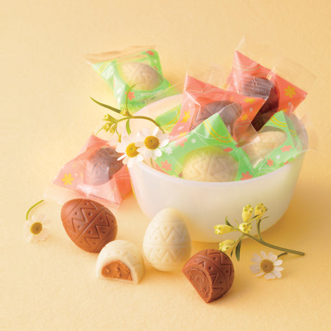 Image shows brown and white chocolate eggs in a bowl with some flowers.