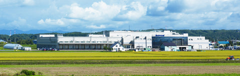 Image shows a factory landscape with greenery and blue skies.