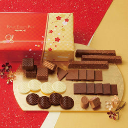 Image shows a red and gold box on the left. Text says ROYCE' Variety Pack ROYCE'. There is a gold tray below with chocolates in confections in various shapes and sizes in the colors of brown and white. Accents include golden flowers.  Background is in red and gold, as split and divided in the middle.