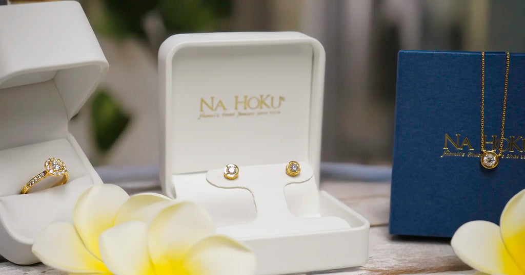 Diamond jewelry set with 'Na Hoku' branding on display with Plumeria flowers.