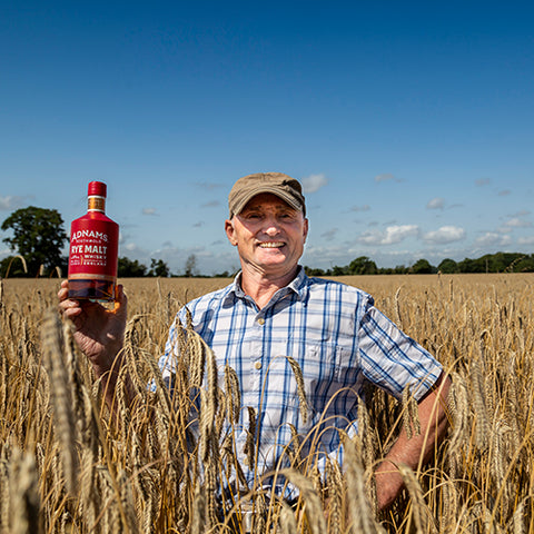 Jonathan Adnams holding a rye whisky bottle in a rye field 