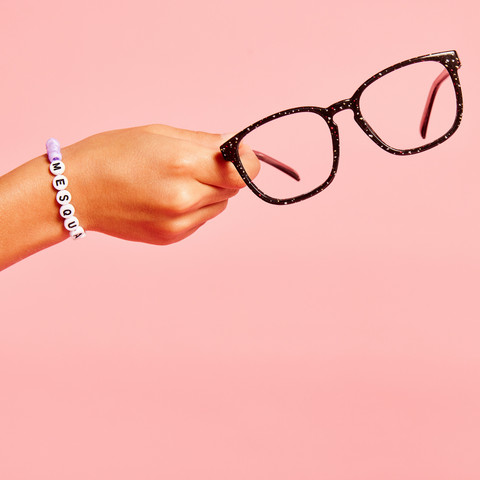 Hand holding black glasses on pink background