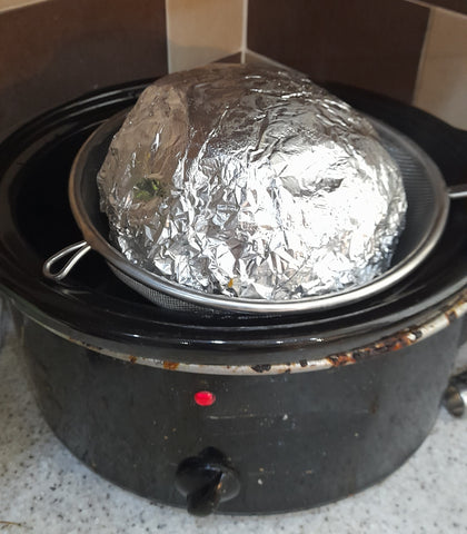 wrapped christmas pudding hovering over a sieve on a slow cooker