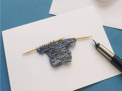 greeting card with a knitted mini jumper on wooden knitting needles