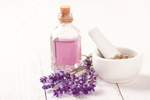 Lavendelblüten neben Mörser und Stößel und Fläschchen mit ätherischem Lavendelöl