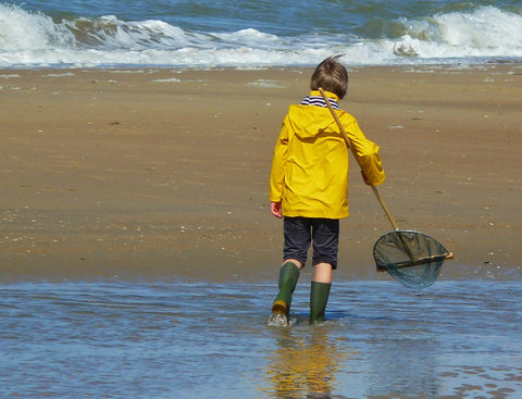 Kind mit gelber Regenjacke und Gummistiefeln am Strand