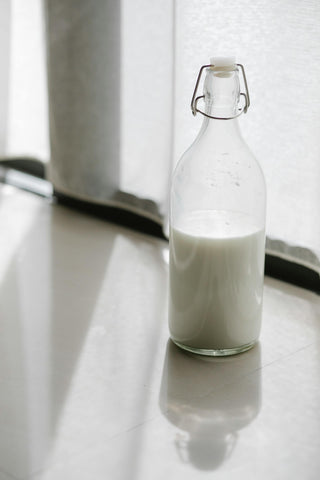 Halbvolle Milchflasche, die am Fenster auf Fliesenboden steht