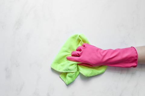 Jemand putzt mit pinkfarbene Gumihandschuh und grünem Mikrofasertuch eine Marmorfläche