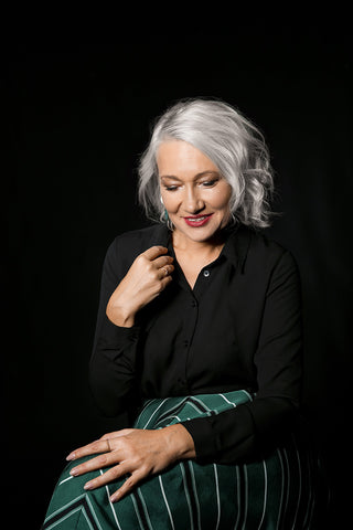 Portrait with black background of a Silver woman sitting and posing wearing a black blouse