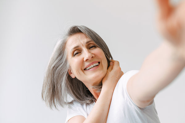 Woman with silver hair leaning to the side holding up left arm and smiling 